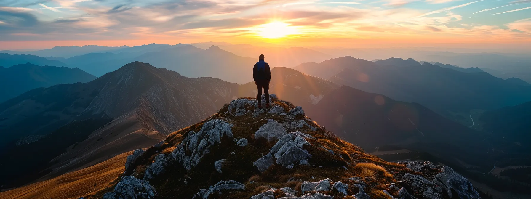 a solitary figure standing atop a rugged mountain peak, gazing out over a vast and majestic landscape at sunset.