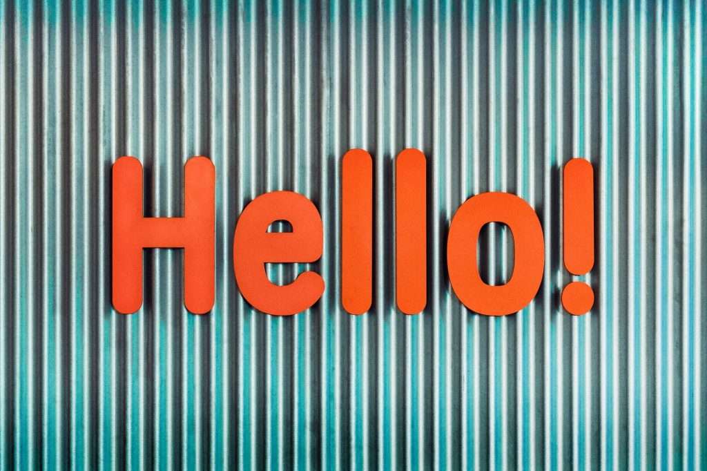 A bright orange 'Hello!' sign stands out against a teal corrugated metal wall.