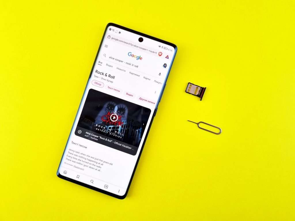 A smartphone with a Google search on a vibrant yellow surface, SIM card, and ejector pin visible.