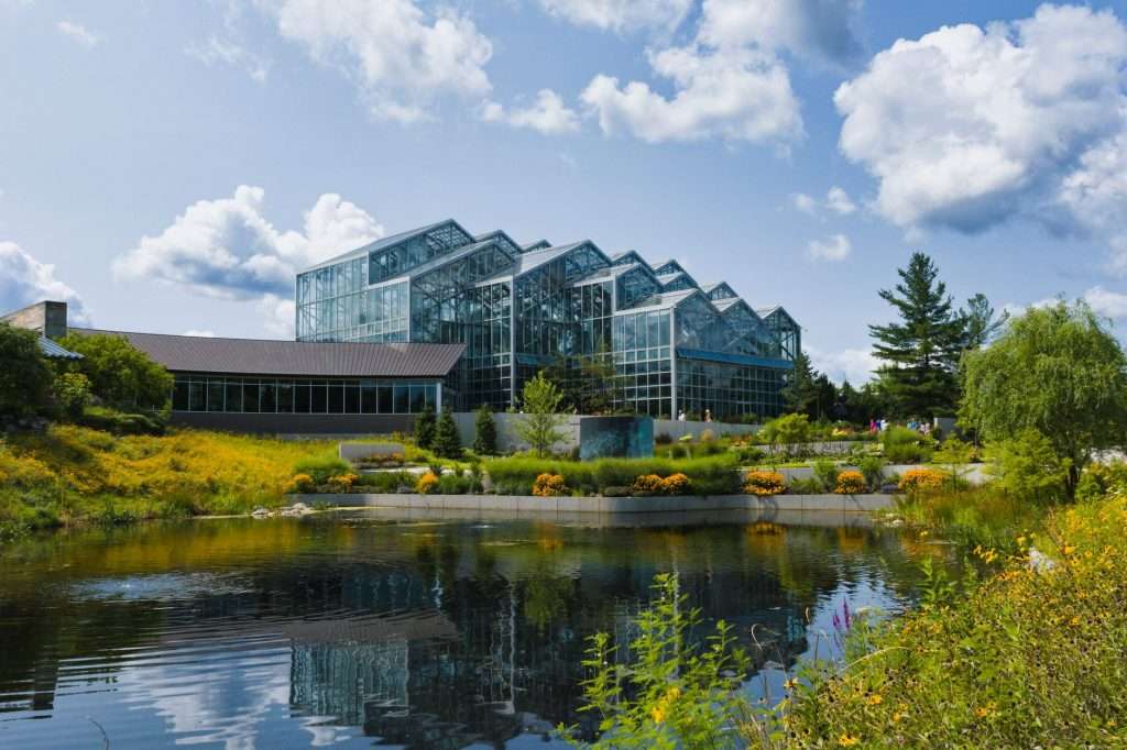 Serene view of the glass conservatory at Frederik Meijer Gardens, reflecting in a calm pond.