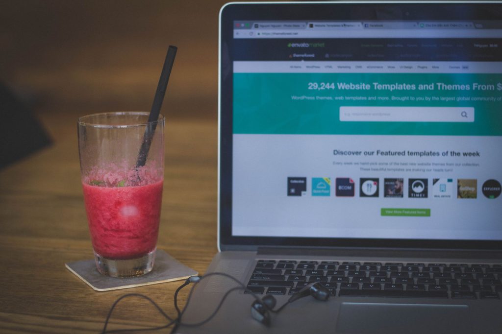 A fruit shake on a desk next to a laptop displaying a website, blending work and refreshment.