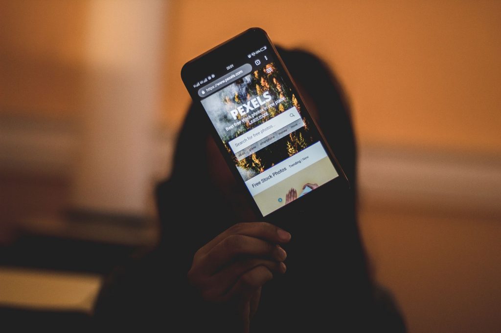 A person holds a smartphone displaying the Pexels website. Ideal for tech and lifestyle themes.