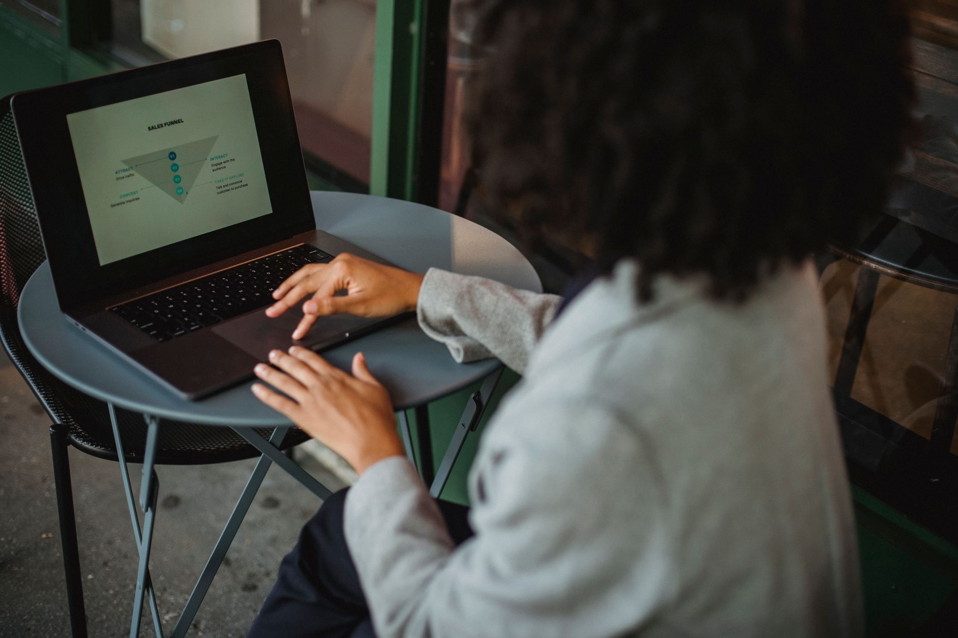 Back view of anonymous ethnic female in suit working with chart on computer while sitting at table in outdoor cafe during …