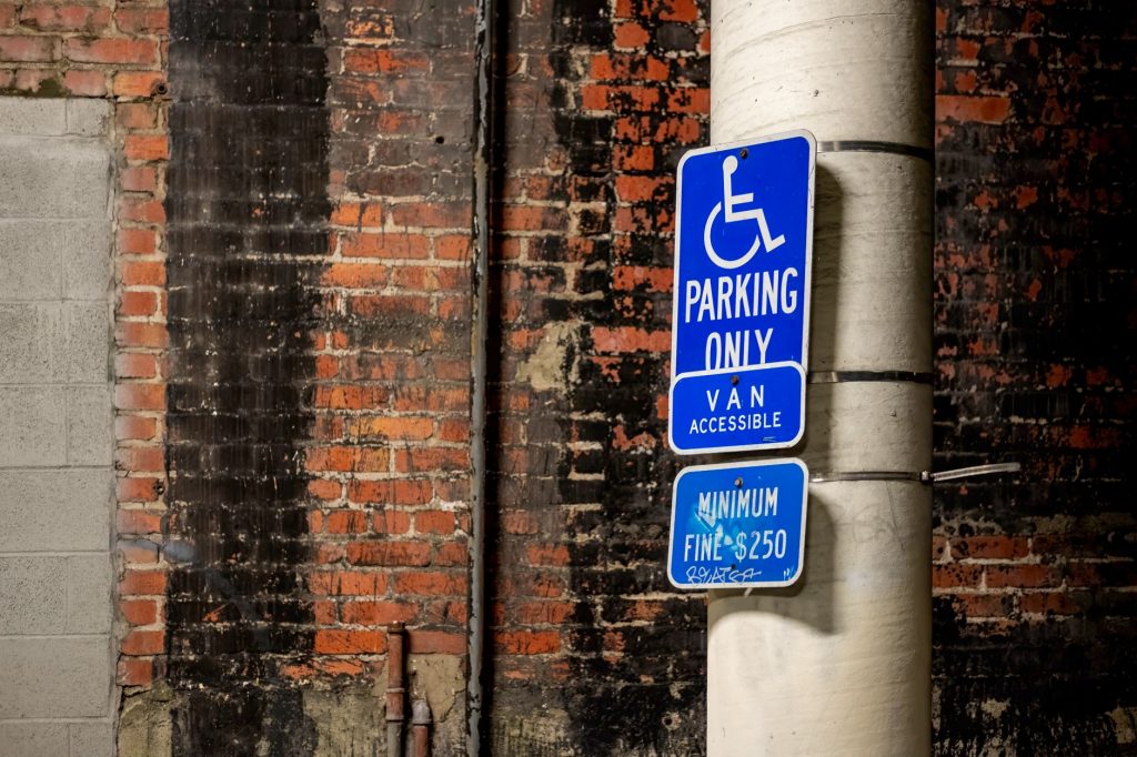 Blue handicap parking sign attached to a pole against a brick wall in the city.