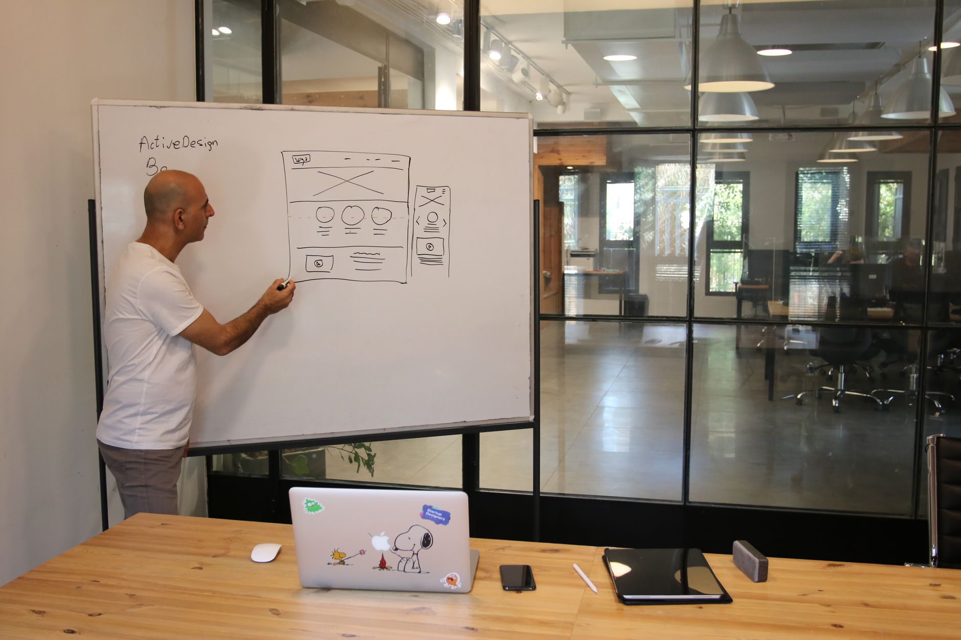 Side view of adult male manager in white t shirt standing near whiteboard and explaining business strategy during work in …