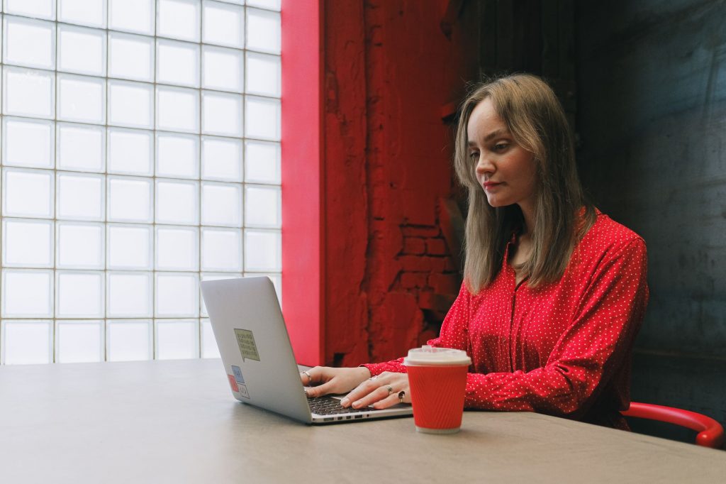 Woman in red blouse focused on work with laptop and coffee indoors.